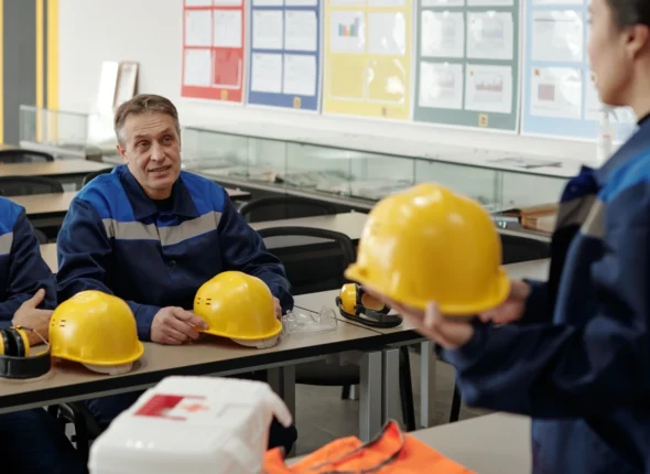Formatrice présentant un casque de chantier à des salariés en tenue de travail, lors d'une formation santé et sécurité