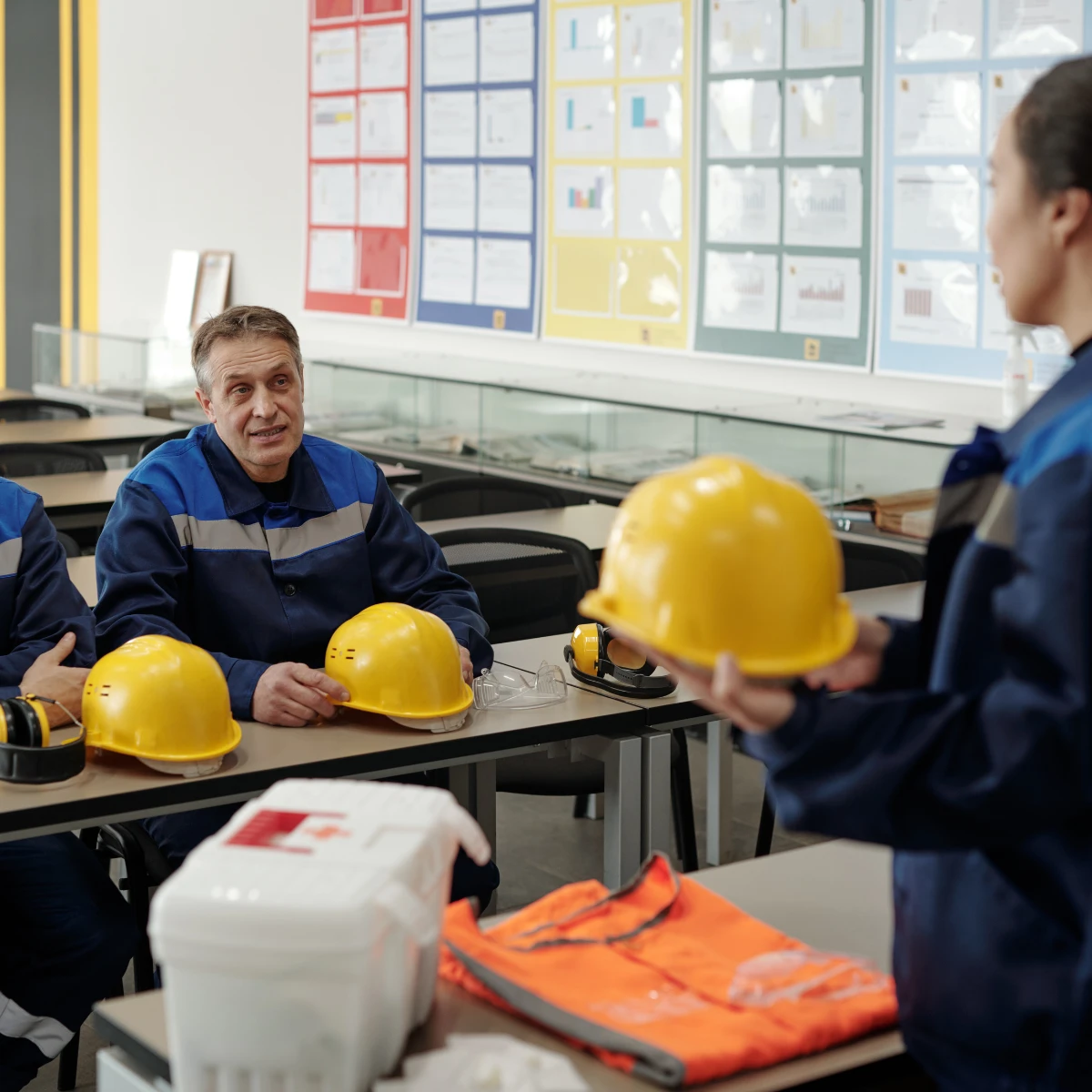Formatrice présentant un casque de chantier à des salariés en tenue de travail, lors d'une formation santé et sécurité